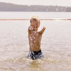 Lächelnder Junge, der Wasser ins Meer spritzt — Stockfoto