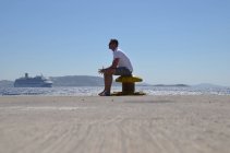 Человек, сидящий на пляже и ожидающий корабль — стоковое фото
