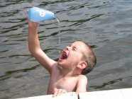 Menino derramando água de garrafa no lago — Fotografia de Stock