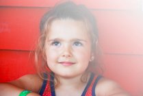 Портрет маленької дівчинки, яка посміхається перед червоною стіною — стокове фото