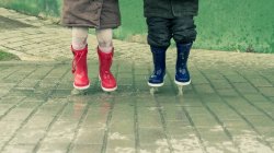 Cropped image of two children jumping in water puddle — Stock Photo