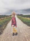 Menina loira em pé na estrada de terra, segurando ursinho de pelúcia e olhando sobre o ombro — Fotografia de Stock
