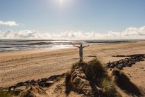 Мужчина с протянутыми руками стоит на песчаной дюне на пляже — стоковое фото