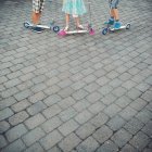Three children standing next to scooters outdoors — Stock Photo
