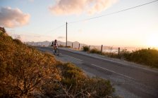 Ciclismo de carretera sobre el mar al atardecer - foto de stock