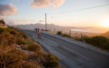 Ciclismo de estrada acima do mar ao pôr do sol — Fotografia de Stock