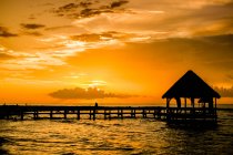 Beau ciel orangé coucher de soleil, eau de mer avec jetée et petite cabane — Photo de stock