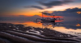 Sanur ist eine Küstenstadt im Südosten der Insel Bali in Indonesien. Sein langer Strand bietet seichtes Wasser. Bunte Jukung-Fischerboote ruhen im Sand, wie hier abgebildet. ein schöner Ort, um den Sonnenaufgang zu verbringen — Stockfoto