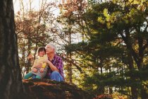 Abuela y nieta sentadas en el bosque abrazándose - foto de stock
