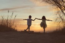 Дівчинка і хлопчик тримають руки, танцюють на заході сонця — стокове фото