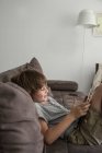 Boy sitting on couch with his digital tablet — Stock Photo