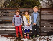 Tre bambini felici in piedi vicino a una recinzione nel giardino — Foto stock