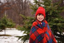 Retrato de una niña envuelta en una manta delante de un árbol de Navidad - foto de stock