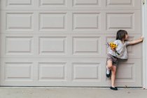 Menina de pé na frente da porta da garagem segurando flores — Fotografia de Stock