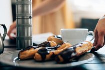 Chocolate eclairs and cup of coffee on tray — Stock Photo