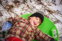 Close-up portrait of Boy lying in a sledge laughing — Stock Photo