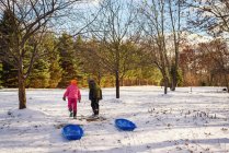 Due bambini che tirano le slitte attraverso la neve — Foto stock