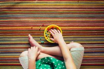 Abgeschnittenes Bild eines Mädchens, das im Schneidersitz sitzt und bunte Snacks isst — Stockfoto