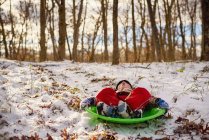 Boy lying in a sledge making a funny face outdoors — Stock Photo