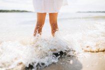 Girl standing on beach with waves splashing her legs, Noosa Heads, Queensland, Australia — Stock Photo
