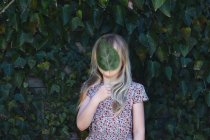 Menina segurando uma folha na frente de seu rosto — Fotografia de Stock