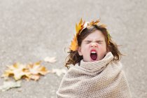 Girl wrapped in a blanket with a wreath of leaves in her hair yawning — Stock Photo