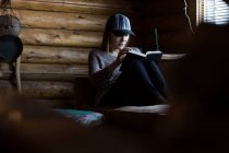 Woman sitting reading book in log cabin — Stock Photo