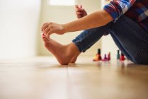 Junges Mädchen sitzt auf dem Boden und lackiert ihre Fußnägel mit Nagellack — Stockfoto