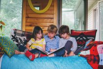 Três crianças sentadas no sofá lendo — Fotografia de Stock