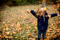 Menino jogando folhas de outono no ar — Fotografia de Stock