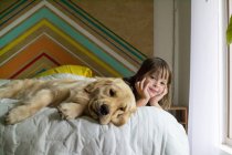 Девочка и золотистая собака-ретривер лежат на кровати — стоковое фото