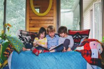 Three children sitting on couch reading — Stock Photo