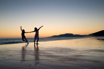Силуэт двух женщин, танцующих на пляже лос Лансес на закате, Фафа, Кадис, Андалусия, Испания — стоковое фото