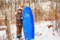 Garçon debout dans la neige tenant un traîneau — Photo de stock