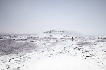 Vista lejana del hombre de pie en el paisaje nevado de invierno, Islandia - foto de stock