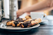 Closeup view of chocolate eclairs and cup of coffee — Stock Photo