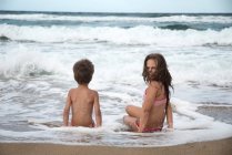 Девушка и мальчик сидят на пляже на краю воды — стоковое фото