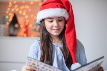 Retrato de uma menina lendo em um chapéu de Natal Papai Noel — Fotografia de Stock