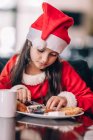 Ragazza in un vestito di Natale Babbo Natale e cappello mangiare la prima colazione — Foto stock