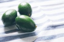 Three avocado fruits on striped tablecloth — Stock Photo