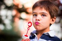 Boy holding bubble wand blowing soap bubbles — Stock Photo