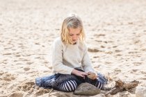 Girl sitting on beach playing with rocks — Stock Photo