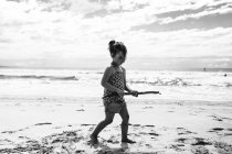 Chica caminando en la playa sosteniendo un palo, Noosa Heads, Queensland, Australia - foto de stock