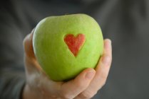Main de femme tenant une pomme verte avec cœur rouge — Photo de stock