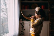 Girl standing in front of window blowing a horn — Stock Photo