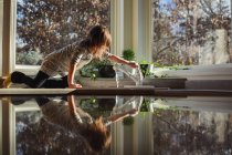 Fille assise sur le comptoir de la cuisine tournant sur le robinet — Photo de stock