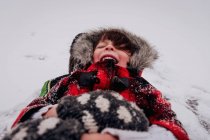 Счастливая девушка в капюшоне, лежащая в снегу — стоковое фото