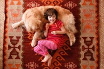 Vista aérea de la niña acostada en el suelo con un perro recuperador de oro - foto de stock
