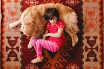 Вид зверху на дівчину, що лежить на підлозі із золотою собакою-ретривером — стокове фото