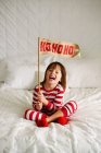 Girl sitting on bed holding a HoHoHo flag — Stock Photo
